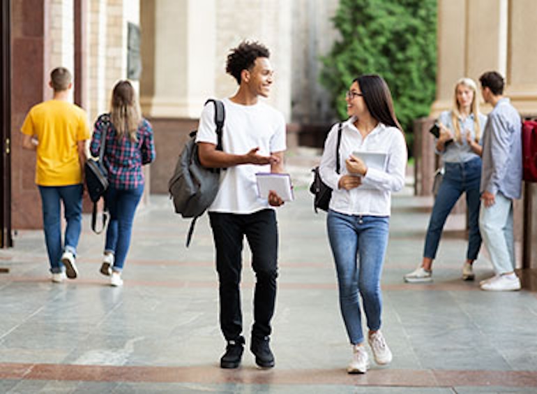 A college-aged male and female student wearing backpacks walking, talking, and smiling